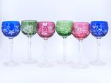 plusieurs verres à vin de différentes couleurs alignés en rang sur une surface blanche