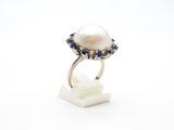une bague ornée d'une perle blanche et d'un saphir, posée sur un socle en marbre blanc