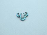 a close up of a turquoise beaded nose piercing on a white surface