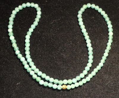 un gros plan d'un collier de perles vertes posé sur une surface noire