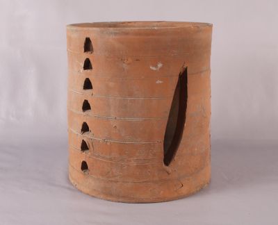 un grand vase marron percé de trous, posé sur une surface blanche