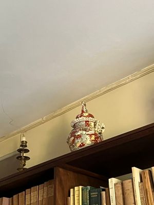de nombreux livres sur une étagère, surmontée d'un vase
