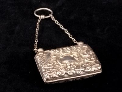 un porte-monnaie ancien en argent, suspendu à une chaîne, sur fond noir