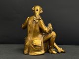 gold statue of a man sitting on a chair with a bird in his lap