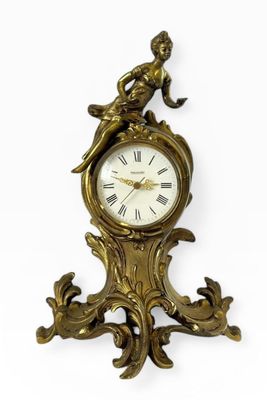 une horloge dorée ornée d'un oiseau sur fond blanc