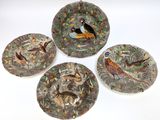 four plates with birds and animals painted on them on a white surface