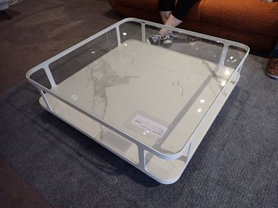 une table basse avec un plateau en verre posée sur un sol recouvert de moquette