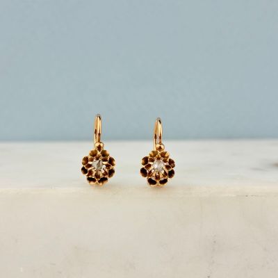 une paire de boucles d'oreilles en or serties de diamants, posées sur une surface en marbre