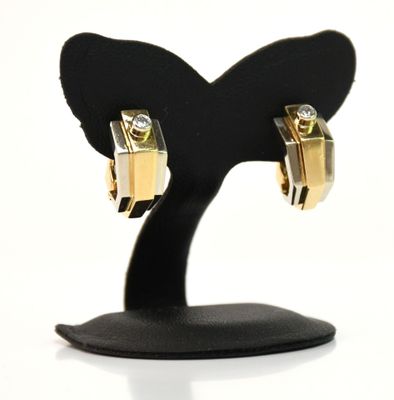 une paire de boucles d'oreilles en or et diamants posée sur un socle noir, sur fond blanc