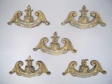 quatre poignées de tiroir en laiton vieilli, ornées de motifs élaborés, sur un fond blanc