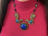 the woman is wearing a pink sweater and a necklace with a blue stone