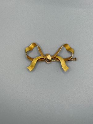 broche en forme de nœud doré avec un ruban torsadé sur fond blanc
