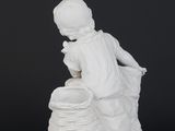 a white figurine of a boy sitting on a rock with a basket
