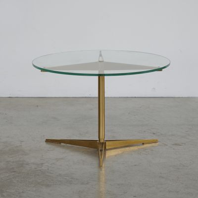 une table ronde en verre avec des pieds en laiton et un plateau en verre