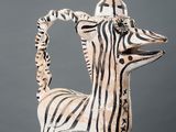 sculpture of a zebra on a white pedestal against a gray background