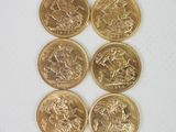 six pièces d'or sont disposées en ligne sur une surface blanche