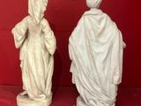two statues of women in white robes are on a red surface