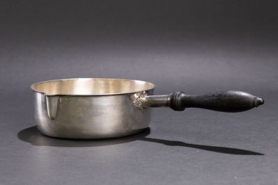 une casserole en argent avec un manche en bois posée sur une table