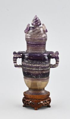 un vase violet posé sur un socle, sur un fond blanc