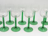 six verres à vin verts sont alignés sur une surface blanche