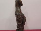 bronze statue of a woman sitting on a stool with her hands on her head