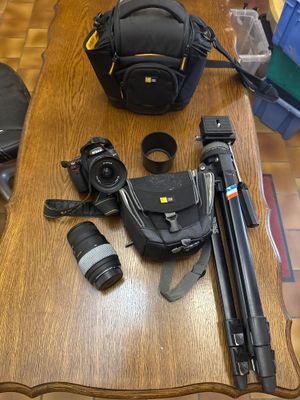une table sur laquelle sont posés un appareil photo, un sac pour appareil photo, un trépied, un appareil photo et un objectif