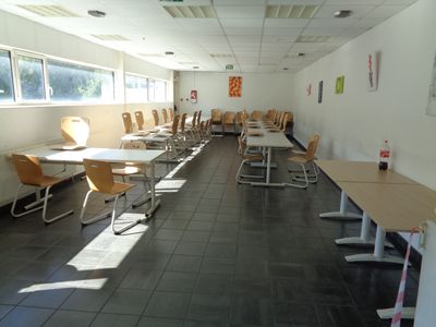 Des tables et des chaises sont alignées dans une longue pièce dotée de fenêtres