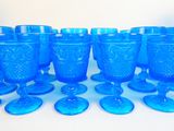 blue glass goblets and cups are lined up on a white surface