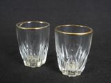 pair of crystal shot glasses with gold rims on a black background