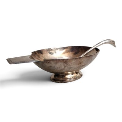 a silver bowl with a spoon in it on a white surface