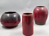 trois vases rouges et noirs posés les uns à côté des autres sur une surface blanche