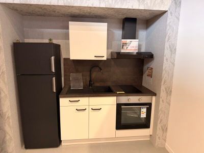 une petite cuisine avec un réfrigérateur noir et des placards blancs
