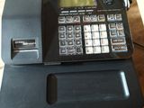 a cash register sitting on a table with a basket of fruit in the background