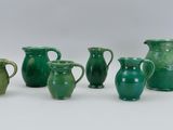 several green vases are lined up in a row on a white surface