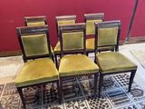 Quatre chaises aux assises recouvertes de velours vert sont disposées devant un mur rouge.
