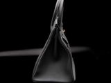 black leather handbag on a black background with a gold clasp