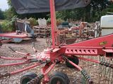 une image représentant un tracteur rouge équipé d'un râteau à l'arrière