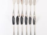 six silverware forks and knives are lined up on a white surface