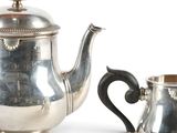 a silver tea pot and a silver cup on a table