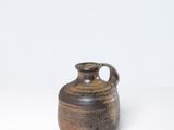 un petit vase brun posé sur une surface blanche