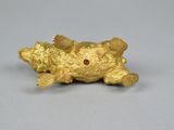 gold figurine of a dog with a red eye laying on its back