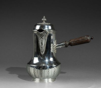 une cafetière ancienne en argent, munie d'une poignée en bois, posée sur une table