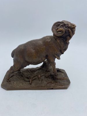 bronze statue of a ram standing on a rock on a white background