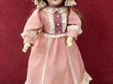 une image représentant une poupée en porcelaine à l'effigie d'une femme vêtue d'une robe rose et d'un bonnet