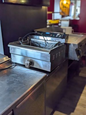 un plan de travail en métal sur lequel est posée une friteuse, dans une cuisine