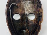 an old wooden mask on a metal stand against a white wall