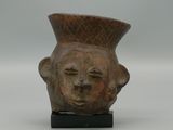 un vase orné d'un visage, posé sur un socle