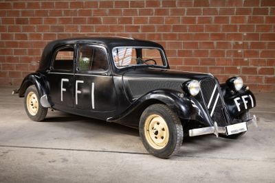 a old black car parked in front of a brick wall