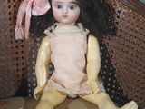 a small doll sitting on a chair with a pink bow on its head