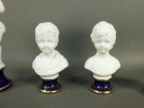 three white porcelain busturines of children on blue pedestals